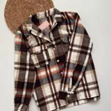 Sobrecamisa a cuadros marrones, blancos y naranjas, con cuello camisero, cierre frontal con botones, dos bolsillos con solapa en el pecho y mangas largas con puños abotonados.