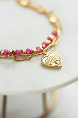 Pulsera dorada de acero quirúrgico con doble cadena, una de eslabones y otra con cuentas rosas. Dije en forma de corazón con ojo grabado y mini cristal.