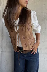 Chaleco de gamuza color camel con estampado floral bordado en tono marrón oscuro y cierre frontal con lazos.