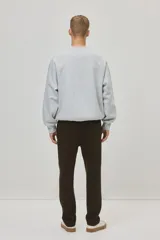 Jogger color marrón oscuro de tejido suave con mezcla de algodón. Presenta pliegues cosidos en la parte delantera, cierre decorativo, cintura elástica con cordón ajustable, bolsillos laterales y un bolsillo insertado en la parte trasera.