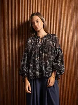 Blusa de gasa con estampado abstracto en tonos oscuros, cuello redondo con lazo ajustable, corte holgado con frunces y mangas largas abullonadas con puños elásticos.