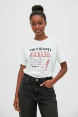 Remera blanca de manga corta y cuello redondo, con estampado frontal gráfico que ilustra un restaurante italiano con el texto Ristorante Bella Notte.