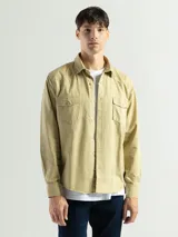 Camisa de manga larga confeccionada en tela canvas de algodón, color beige. Presenta cuello clásico, cierre frontal con botones y dos bolsillos frontales con tapa.