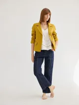 Blazer de lino color mostaza, inspirado en la sastrería clásica, con corte estructurado, solapas con pespuntes decorativos, cierre frontal con botones y bolsillos con tapa.