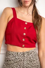 Top corto color rojo, con escote cuadrado y tirantes anchos. Presenta una hilera de botones marrones en el centro del frente.