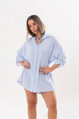 Vestido camisero de lino color celeste, con escote en V, cuello clásico, cierre frontal de botones y mangas tres cuartos regulables. Diseño holgado con corte asimétrico.