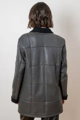 Campera de cuero color tostado con diseño de paneles, cuello alto y puños con forro de corderito sintético. Presenta cierre frontal con botones grandes y bolsillos laterales.