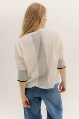 Buzo de punto en color negro con mangas tres cuartos y puños en contraste color marrón. Presenta un diseño holgado con tajos laterales y un aplique circular con logo en la parte inferior.