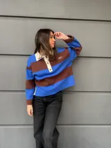 Buzo tipo rugby de algodón con diseño de rayas horizontales anchas en azul y marrón. Presenta cuello polo en color crema con cierre frontal de tres botones y mangas largas.