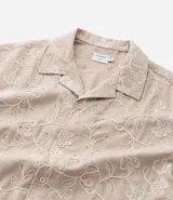 Camisa de poliéster color beige con bordado floral blanco, de corte regular, cuello inglés, manga corta y abotonada en el frente.