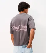 Remera gris oscuro de corte oversized con cuello redondo y manga corta. Cuenta con estampa frontal en color rosado con texto "LEAD THE WAY", tres estrellas y grafismo de números.