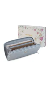 Billetera larga con cierre perimetral, confeccionada en material símil cuero con textura rugosa. Cuenta con placa metálica decorativa en el frente y múltiples compartimentos internos para tarjetas, billetes y monedas.