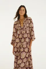 Vestido largo de bordó con estampado ornamental en tonos rosados y dorados, mangas tres cuartos abullonadas con puños elásticos, escote en V con cordones y falda escalonada con vuelo.