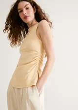Musculosa de punto color beige con diseño sin mangas, cuello redondo y detalle de fruncido lateral.