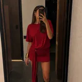 Vestido corto rojo de manga corta con hombreras, diseño holgado en la parte superior y falda drapeada ajustada con un detalle de anudado lateral y larga tira colgante.