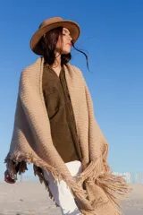 Poncho beige de tejido de punto con flecos y cuello alto.
