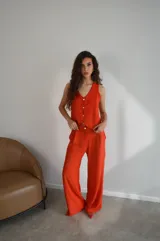Conjunto de dos piezas compuesto por un chaleco sin mangas con cierre frontal de botones y un pantalón de corte recto y tiro alto, confeccionado en tela crepe color naranja.
