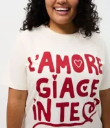Remera de algodón de corte holgado y largo, con cuello redondo y mangas cortas. Presenta una estampa frontal con la frase 'L'AMORE GIACE IN TE' en color rojo sobre fondo crema.