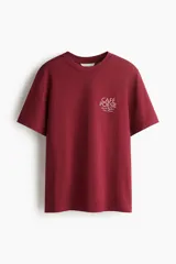 Remera de manga corta color bordó, con cuello redondo y corte holgado. Presenta un pequeño estampado blanco en el pecho con el texto "CAFÉ POÉSIE" y una dirección en París, Francia.