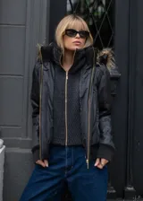 Campera negra de estilo urbano con diseño acolchado, cierre frontal dorado y cuello alto con textura. Incluye capucha con borde de piel sintética y puños de tejido acanalado.