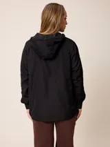 Campera de corte recto y estilo funcional, color beige, con capucha integrada, cierre frontal con botones a presión y bolsillos delanteros amplios. Presenta un diseño minimalista con cordones ajustables en la capucha.