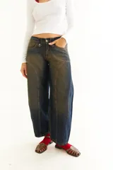 Jean de corte balloon y tiro bajo, con diseño de recortes curvos en las piernas, cierre de botones en la cintura y acabado desgastado en tonos azul y marrón.