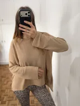 Sweater de punto color beige, con cuello redondo, mangas largas y diseño holgado con aberturas laterales en el ruedo.