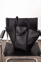 Bolso tote negro de cuero con doble asa de mano y cierre superior.