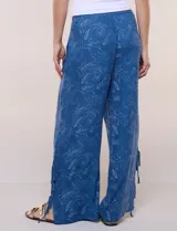Pantalón palazzo de rayón color azul con estampado paisley blanco, corte amplio, tiro medio-alto con pretina elastizada y aberturas laterales en el puño regulables con lazos.