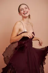 Vestido corto bordó de seda, con tirantes finos, cuerpo drapeado y falda con volados.