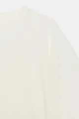 Camiseta tipo capa oversize de color blanco, confeccionada en hilatura de algodón 100%. Presenta cuello redondo, manga corta y un diseño de bajo asimétrico con caída pronunciada en uno de los laterales.