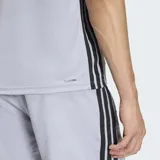 Remera deportiva Adidas de manga corta, color gris claro, con cuello redondo y diseño de las tres rayas características de la marca en color negro sobre los laterales. Presenta el logo de la marca en el pecho.