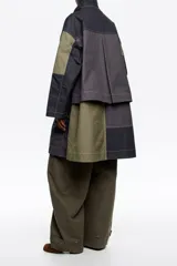 Gabardina midi de algodón con diseño patchwork en tonos azul marino, gris y verde oliva. Presenta cuello de pana, cierre frontal con botones a presión y gancho metálico, bolsillos laterales con solapa y costuras a la vista.