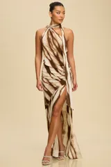 Vestido largo de satén con estampado abstracto en tonos marrones y beige. Presenta un diseño asimétrico con cuello halter tipo corbatín, espalda descubierta y un tajo profundo en la pierna con detalle drapeado en la cadera.