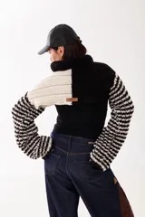 Polera corta de tejido artesanal con diseño bicolor en blanco y negro. Presenta cuello alto, mangas largas con trama a rayas y etiqueta de marca en la parte posterior.