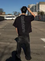 Remera negra oversize de manga corta, con estampa tipográfica vertical en la espalda y logo pequeño en el frente.