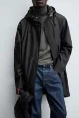 Parka de tejido con acabado engomado, diseño de corte recto y largo medio. Presenta cuello subido con capucha ajustable, cierre frontal con cremallera oculta bajo solapa con botones a presión, mangas largas y bolsillos laterales de vivo.