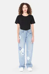 Pantalón de jean celeste con apliques florales geométricos en tonos azules y blancos.