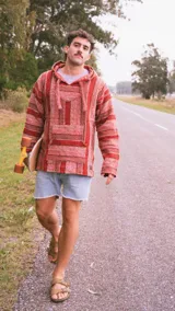 Buzo con capucha de algodón tejido a rayas horizontales en tonos rojo y marrón. Tiene un bolsillo tipo canguro en el frente y cordones ajustables en el cuello. Diseño holgado y estilo relajado.