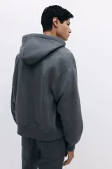 Campera con capucha de tejido pesado de mezcla de algodón, color gris oscuro jaspeado, con interior cepillado suave. Modelo con hombros caídos, capucha forrada en punto con cordón para ajustar, cierre frontal y bolsillos canguro. Puños y bajo acanalados. Corte oversized.