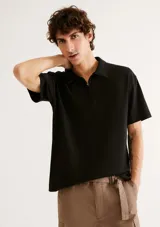 Remera polo negra de manga corta, con cuello camisero y cierre frontal parcial.