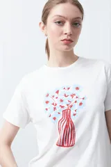 Remera blanca de manga corta con estampado frontal de un florero rojo con rayas verticales y un ramo de flores azules y rojas.