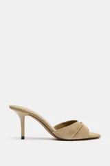 Sandalia de tacón destalonada estilo mule en piel, de color beige, con tira ancha delantera y tacón alto fino.