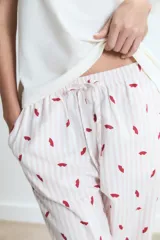 Pijama compuesto por una remera de cuello redondo en color blanco con un pequeño estampado de labios rojos en el pecho y un pantalón largo de corte holgado con estampado de rayas verticales y labios rojos sobre fondo claro.