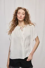 Camisa de manga corta color celeste, confeccionada en viscosa fluida, con silueta amplia y escote redondo con frunces y lazo para anudar.
