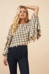 Chal tipo poncho de lana fina sin teñir, con estampado a cuadros en tonos beige y marrón. Presenta cuello bote, aberturas laterales para los brazos y terminaciones desflecadas.