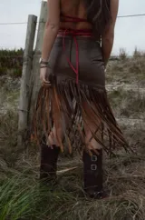 Pollera midi de cuero marrón con diseño asimétrico y flecos largos que aportan movimiento y textura.