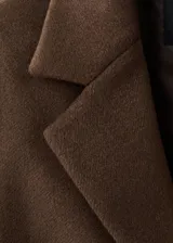 Abrigo de paño en color marrón, con diseño de doble botonadura, cuello con solapas y bolsillos laterales con solapa.