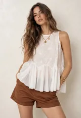 Blusa sin mangas de color blanco, confeccionada en tejido semitransparente con detalles bordados en el pecho y diseño de volados en la parte inferior.