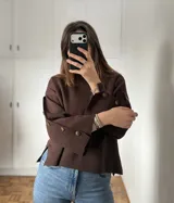 Sweater de bremer color chocolate con cuello alto y mangas largas con detalle de botones en los puños. Presenta un diseño holgado con aberturas laterales en el ruedo.
